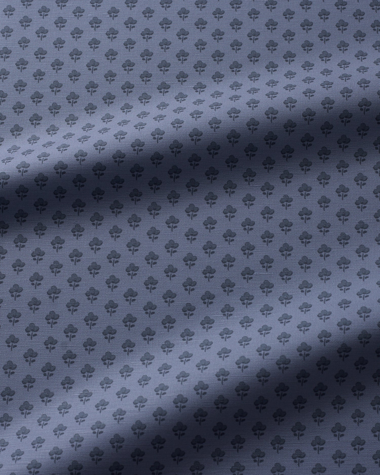 A close-up of a fabric surface with a repeating small floral pattern in a muted blue-gray tone, with soft diagonal shadows across the material.