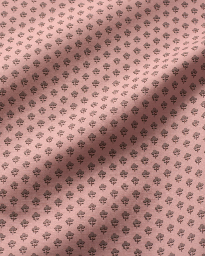 A close-up of a dusty pink fabric with a repeating dark gray floral or rose pattern, featuring soft diagonal shadows across the surface.